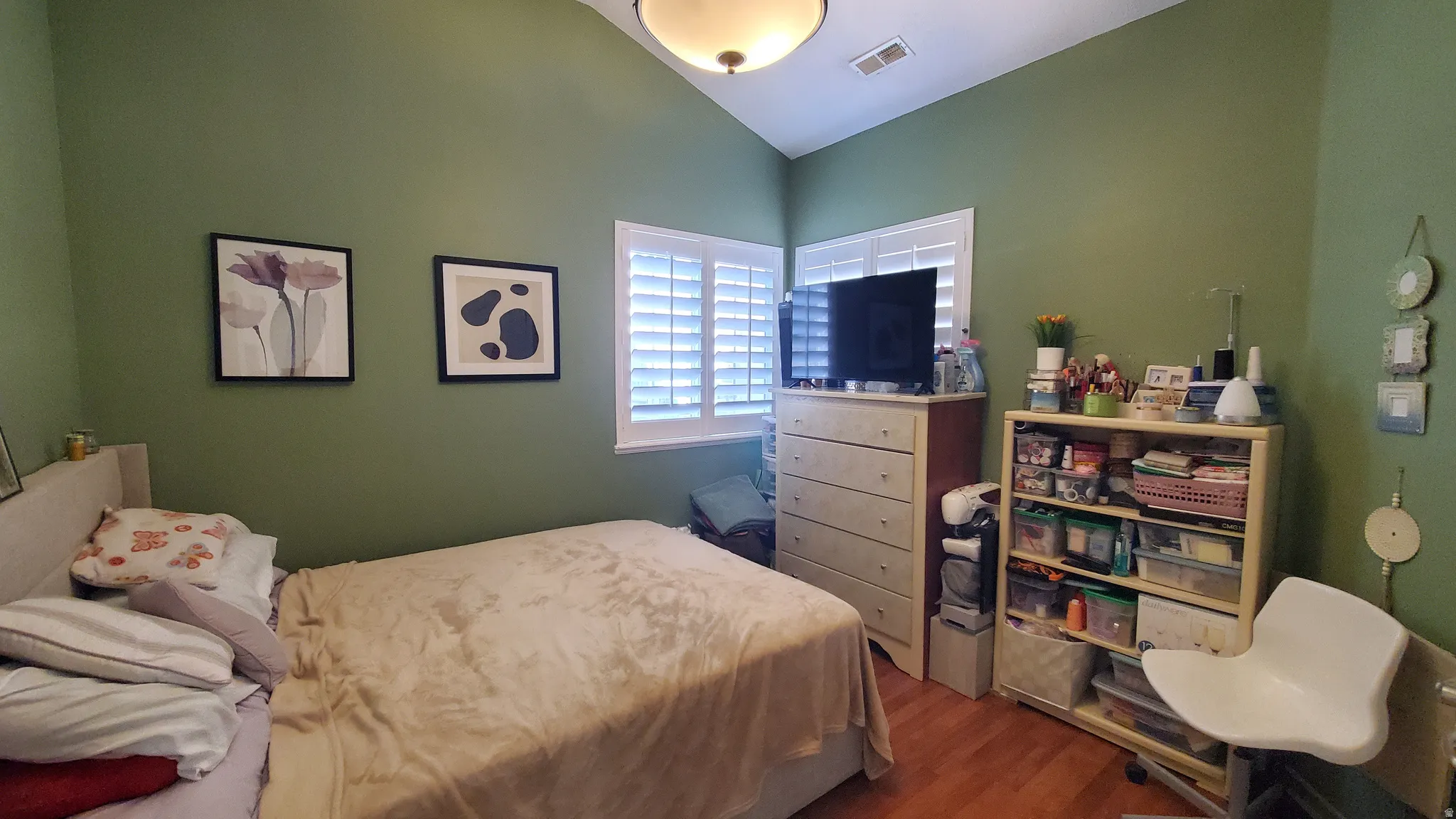 Room with vaulted ceilings, wood-finish flooring, and a window featuring white plantation shutters