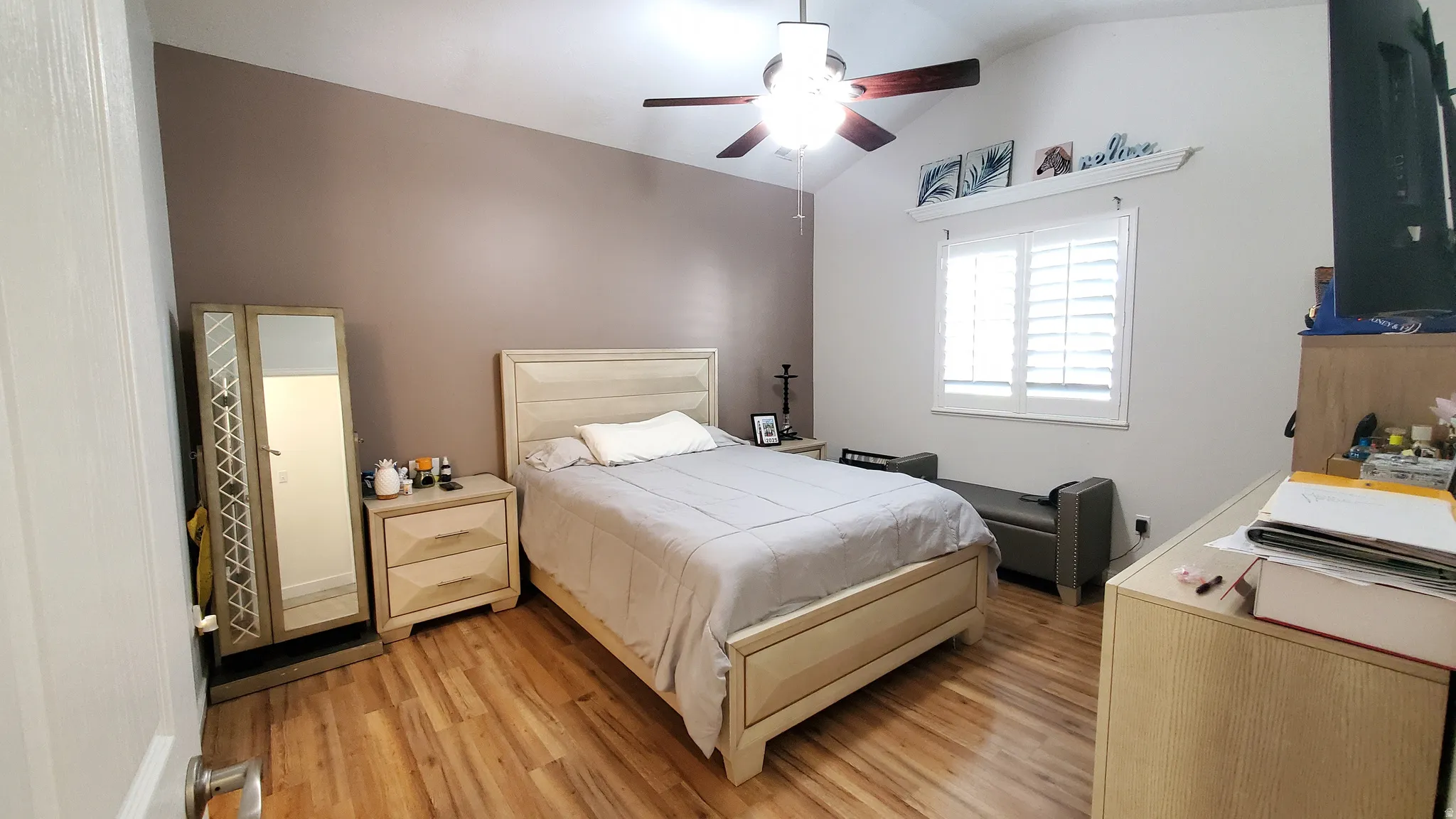 Vaulted ceiling with a ceiling fan, wood-finish flooring, plantation shutters, and a feature wall