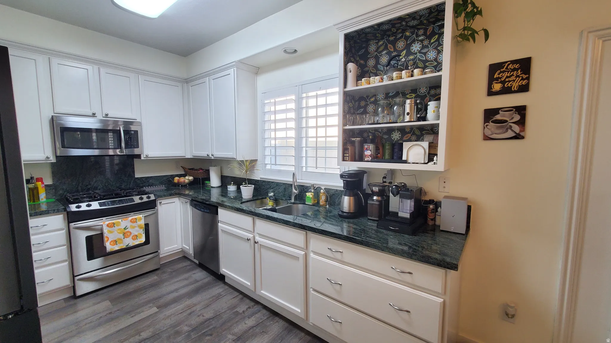 Kitchen featuring wood-finish flooring, white cabinetry with silver-tone hardware, dark green countertops, a stainless steel gas range, and a stainless steel over-the-range microwave