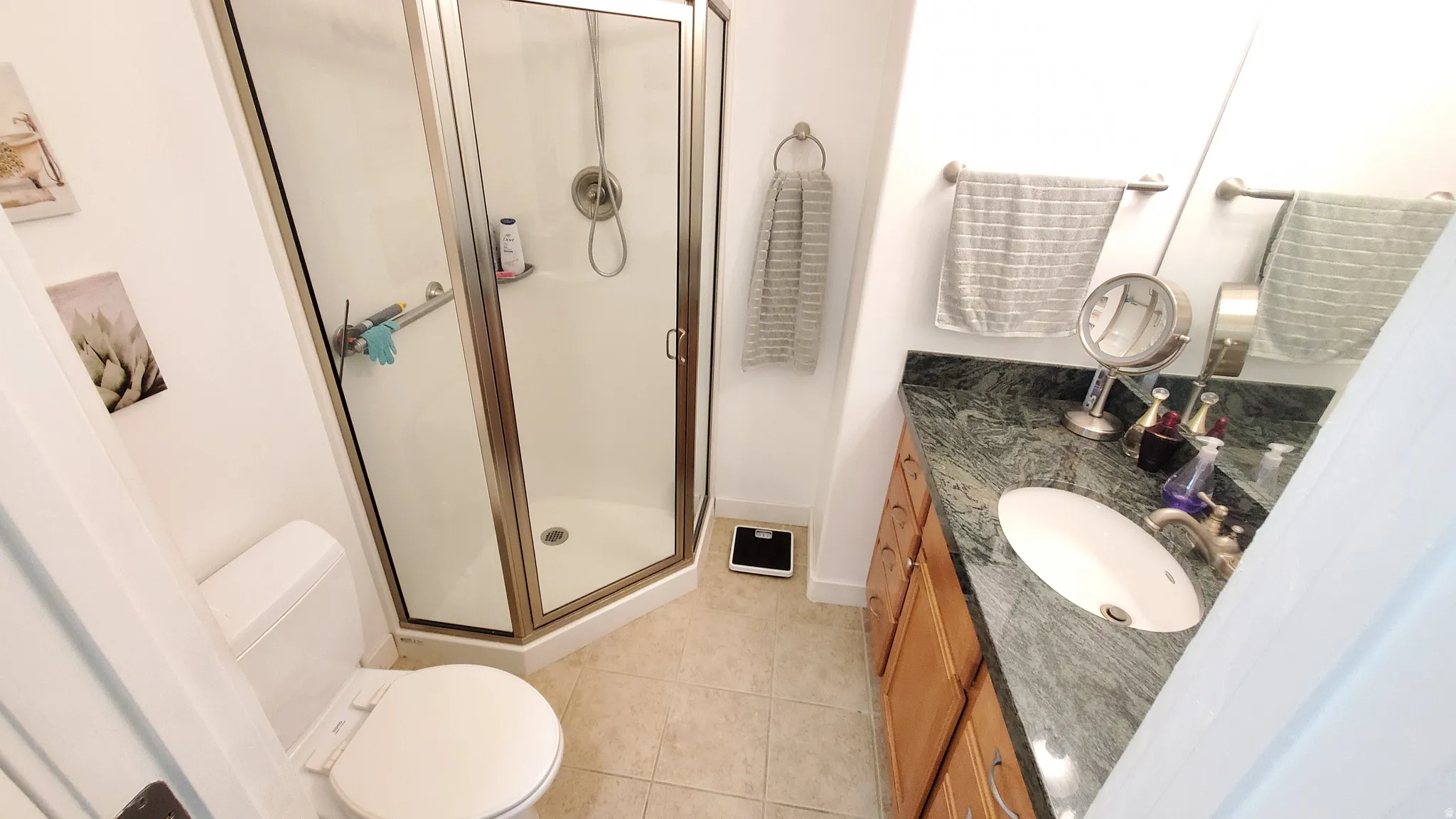 Bathroom featuring an enclosed corner shower, a single vanity with a dark green patterned countertop, and light wood cabinetry