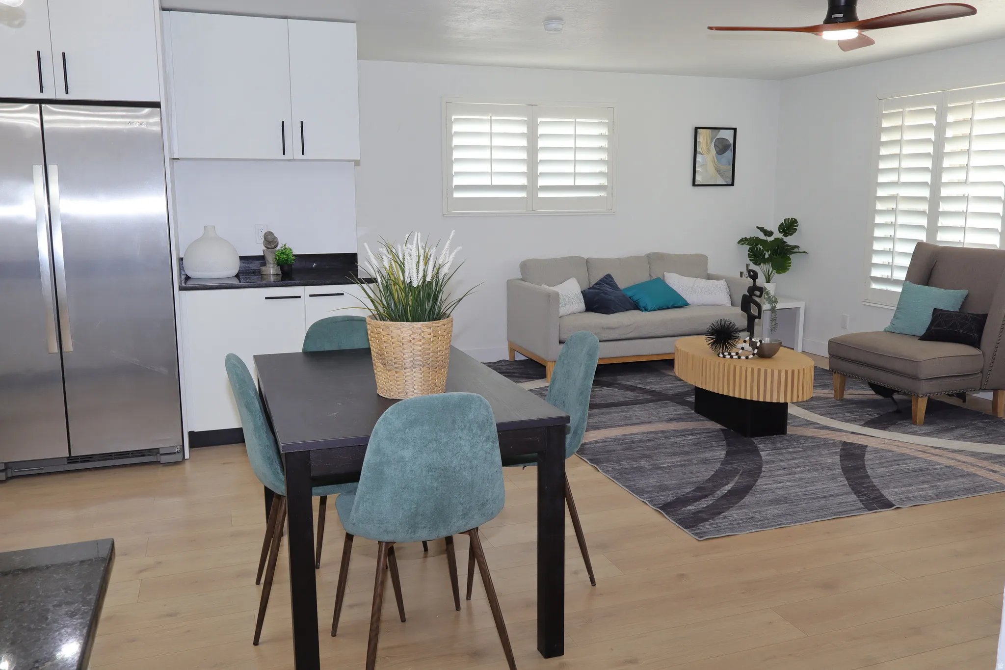 Open-concept living area featuring a modern ceiling fan, light wood-finish flooring, and white plantation shutters