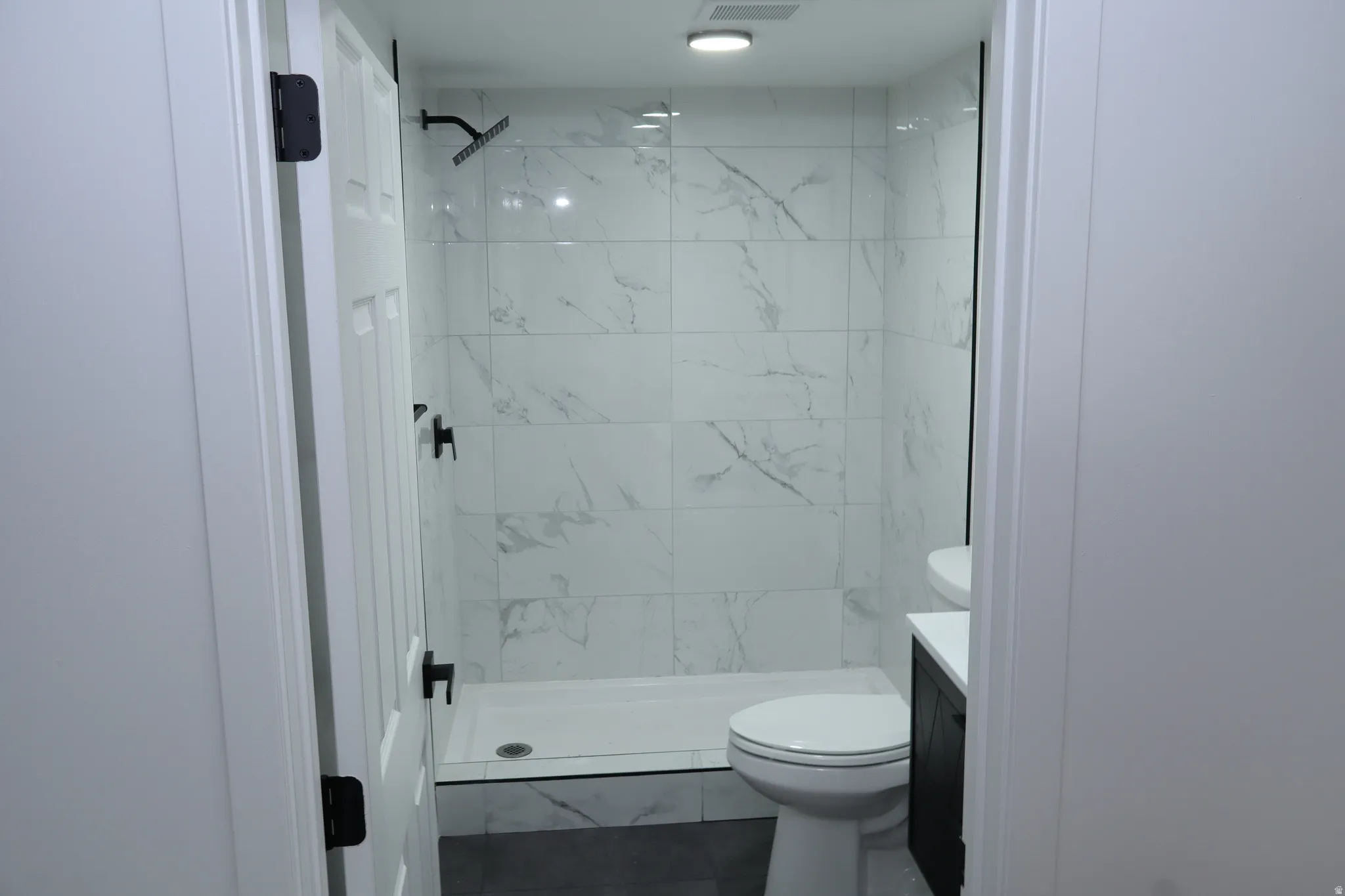 Modern bathroom featuring a tiled shower with matte black fixtures, a white shower pan, a wall-mounted toilet, and a dark wood-finish vanity with a white countertop and vessel sink