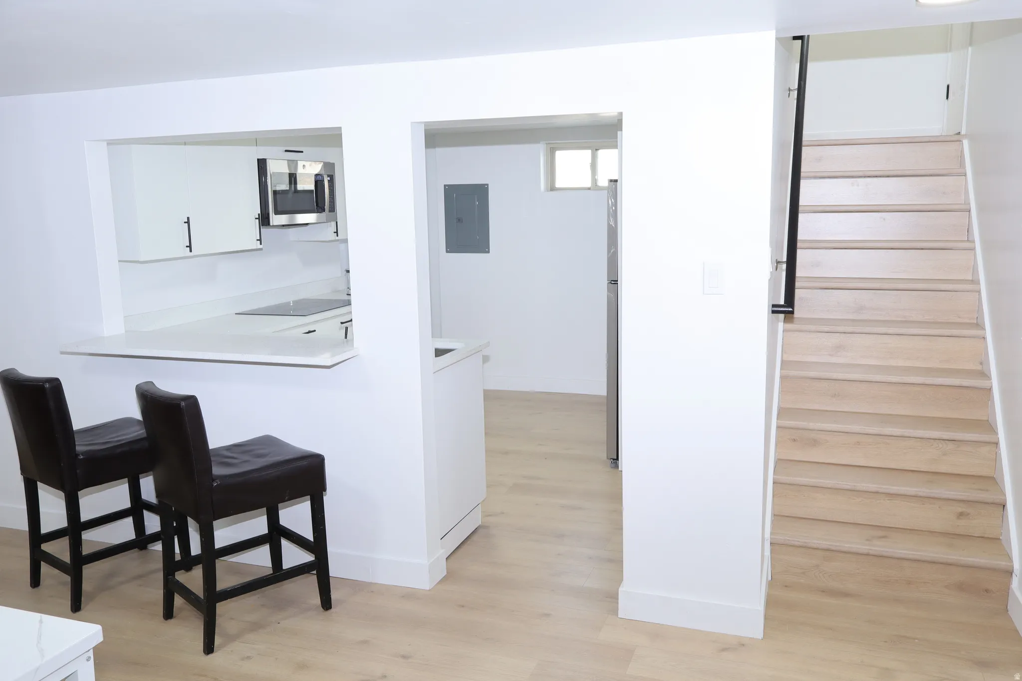 Open-concept living space featuring wood-finish flooring, a contemporary kitchen pass-through with a breakfast bar, white cabinetry with black hardware, and stainless steel appliances