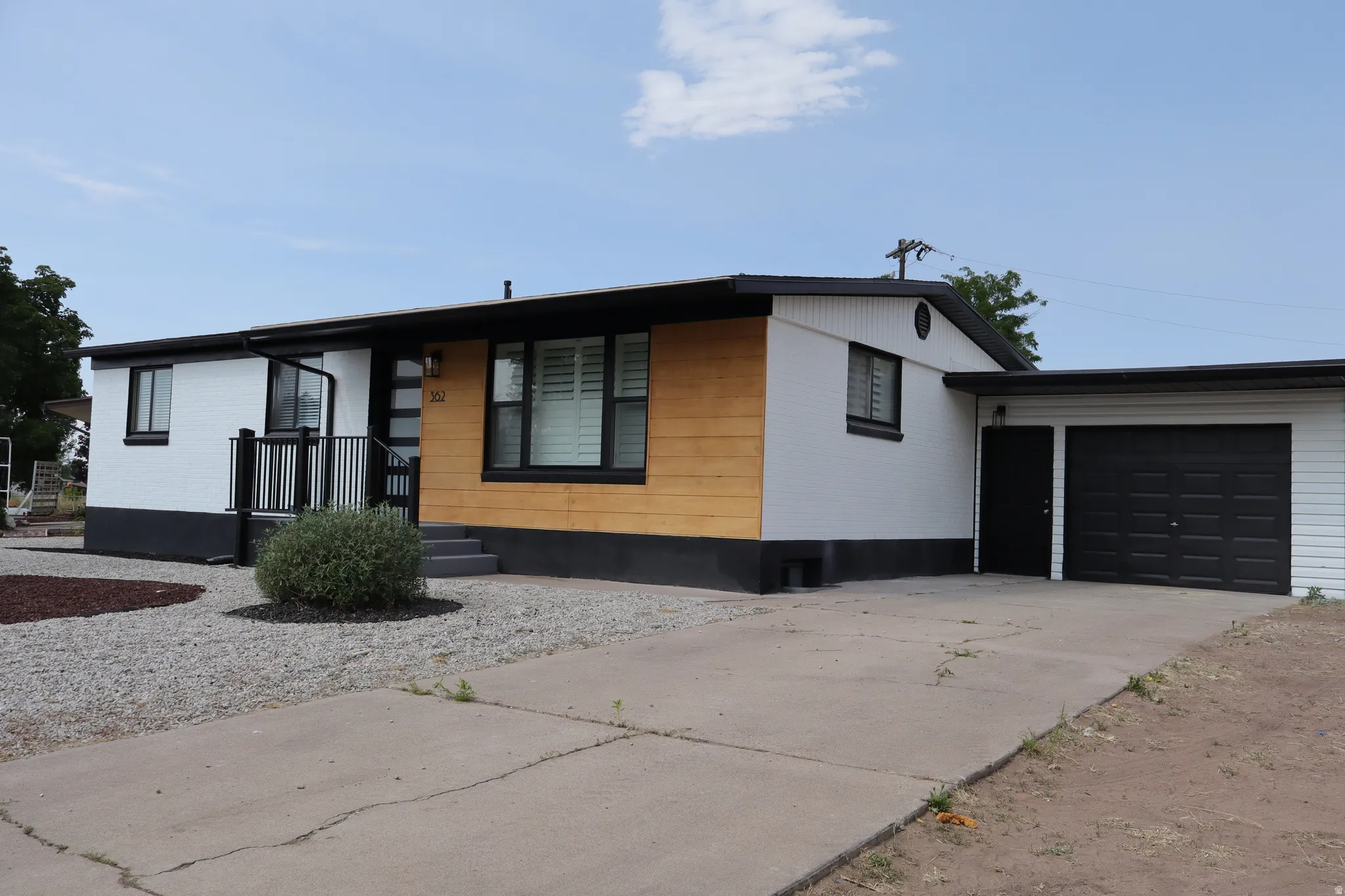 Modern exterior featuring white siding with black trim and a natural wood-finish accent panel