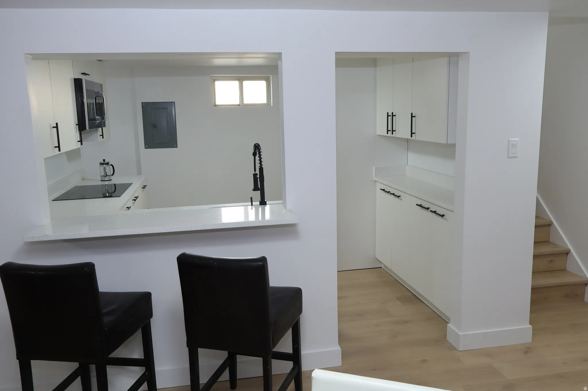 Kitchenette featuring a pass-through counter, white cabinetry with dark hardware, a built-in cooktop, and a wall-mounted microwave