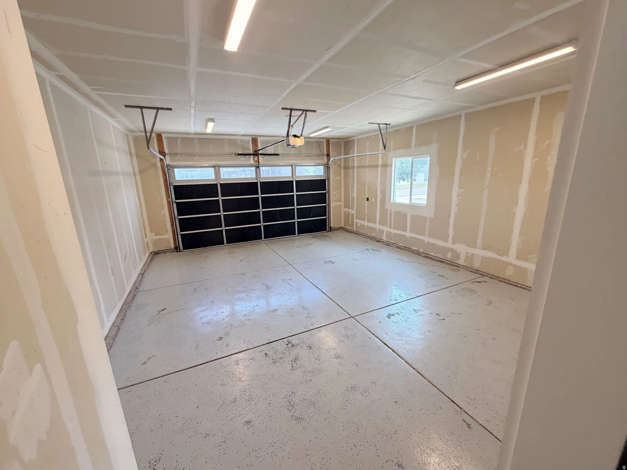 Spacious garage featuring a two-car overhead door with frosted panels, a concrete floor, and multiple overhead fluorescent light fixtures