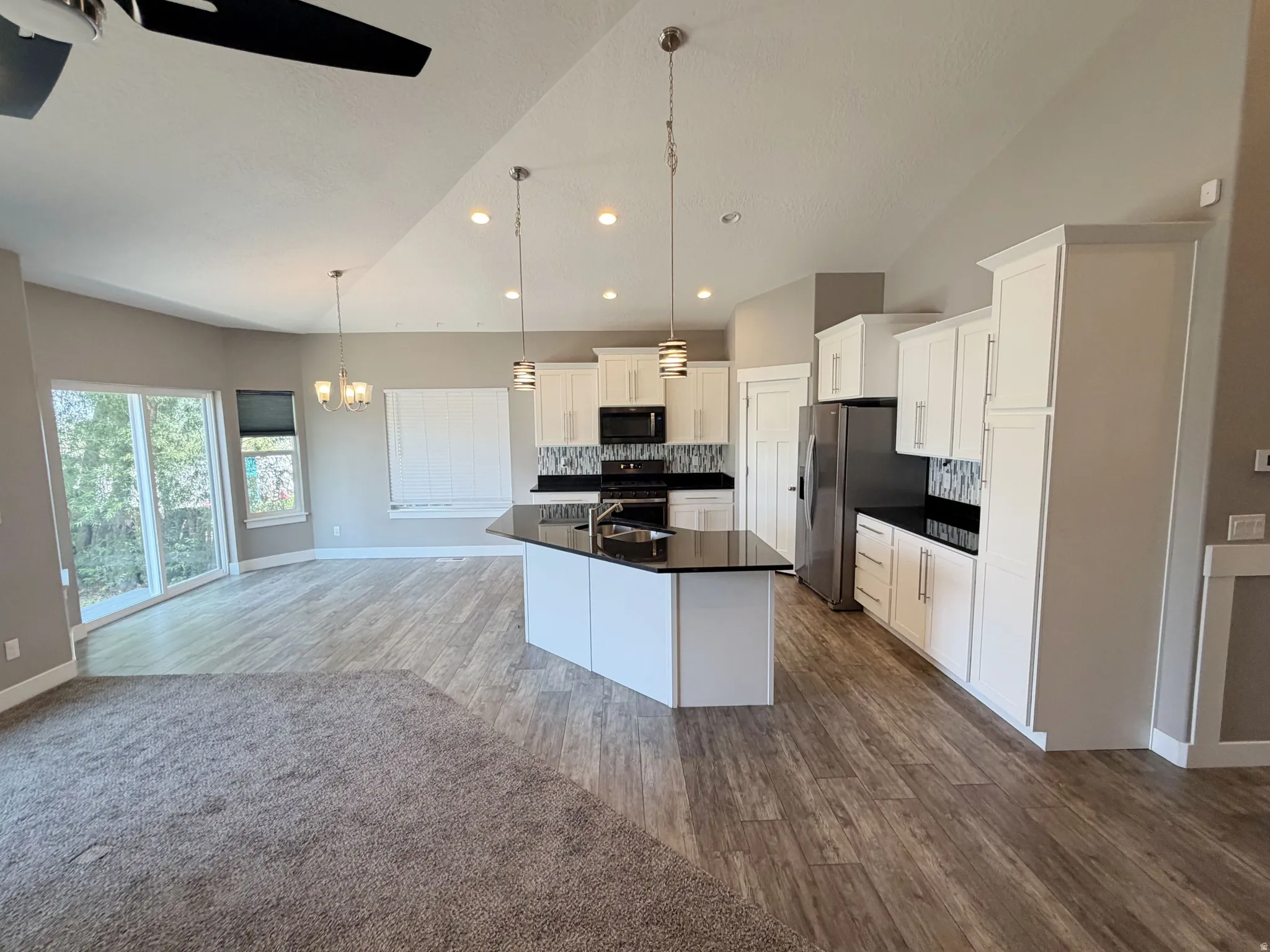 Open-concept living space featuring a kitchen island with black countertop, white cabinetry, stainless steel appliances, and a mosaic tile backsplash