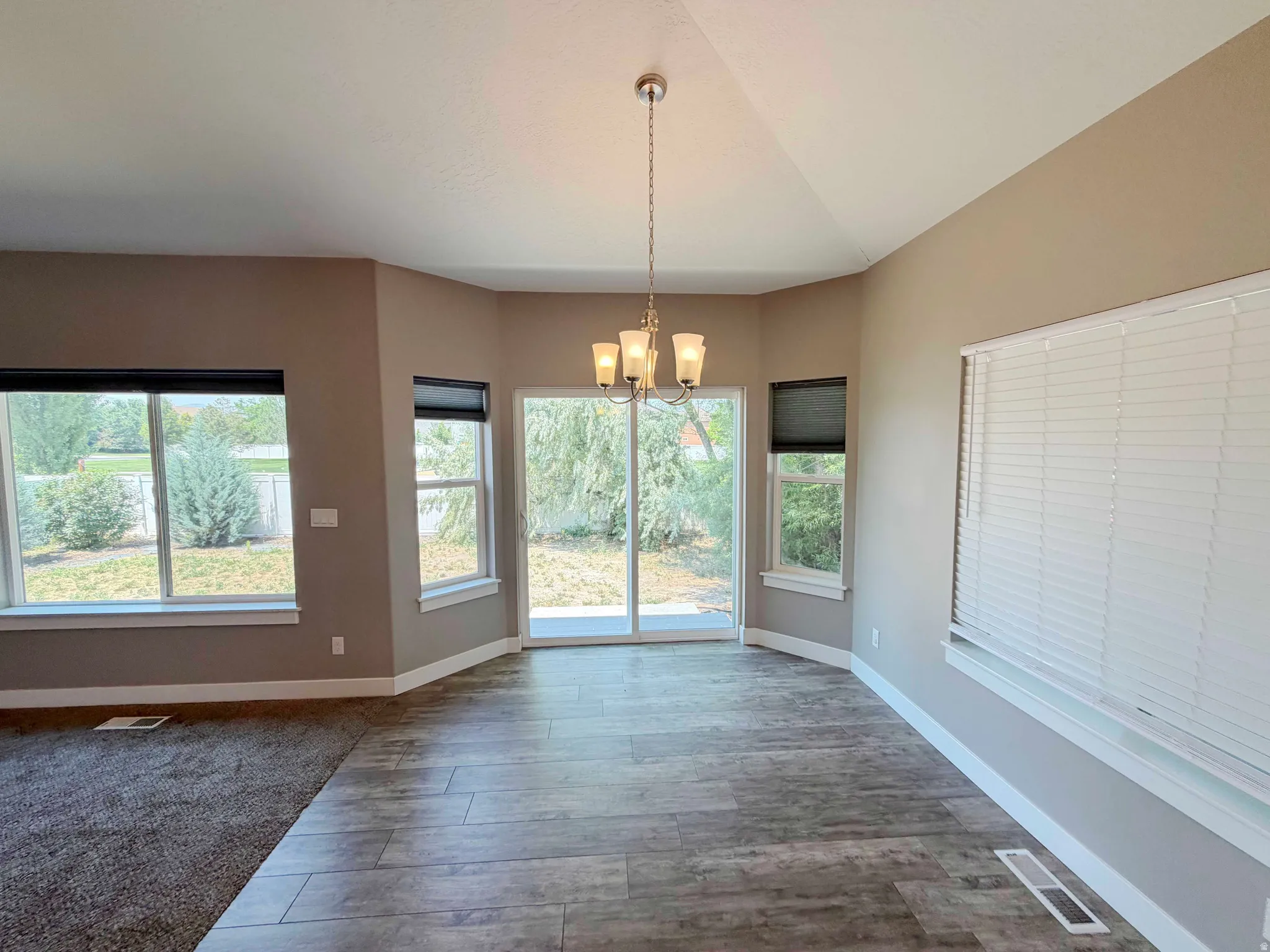 Open-concept area featuring wood-finish flooring, a contemporary chandelier, vaulted ceilings, and a sliding glass door leading to the exterior