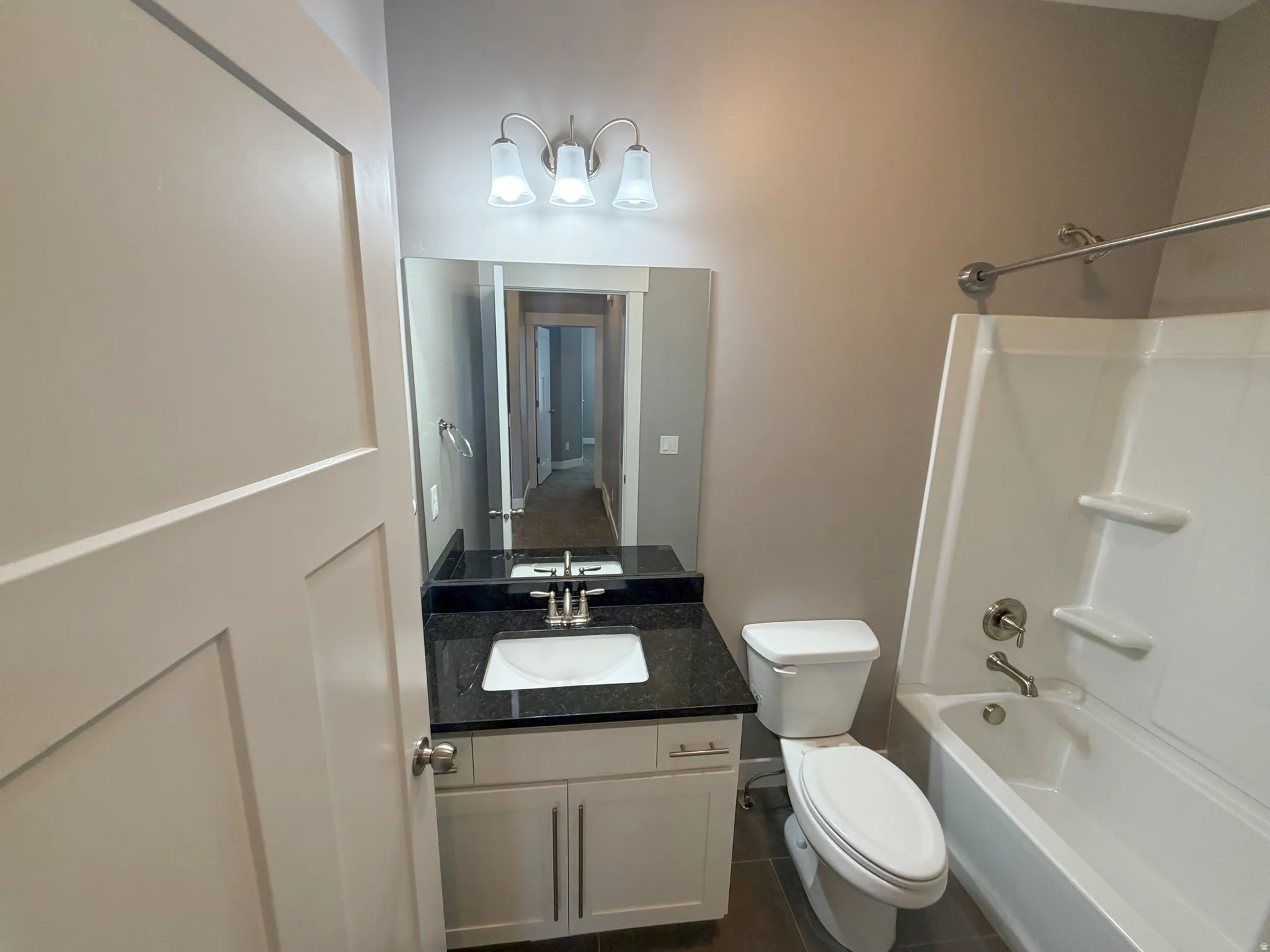Full bathroom featuring a white vanity with dark stone countertop, integrated sink, and brushed nickel faucet