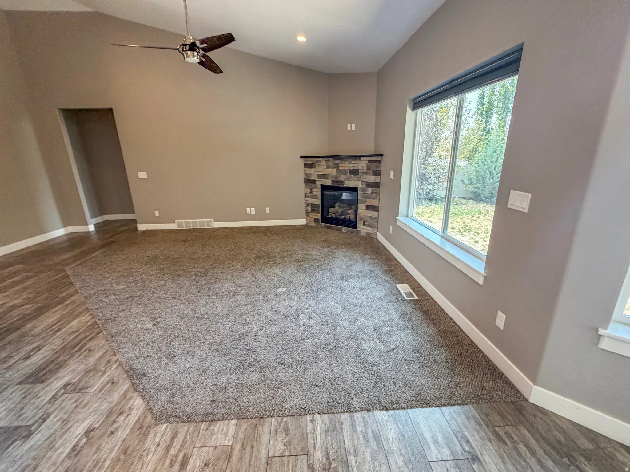 Spacious room featuring vaulted ceilings, a contemporary ceiling fan, and a corner fireplace with a stone surround