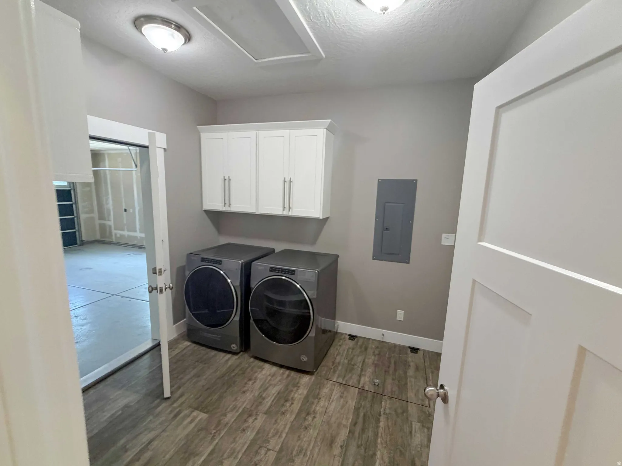 Utility room featuring wood-finish flooring, overhead cabinetry, ceiling-mounted lighting, and a solid core door