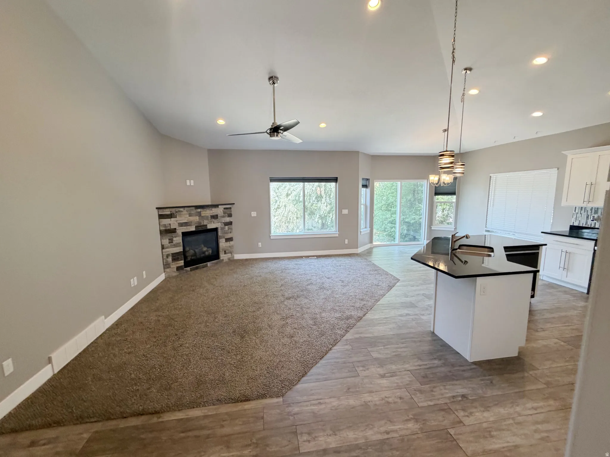 Open-concept living space featuring a stone-faced fireplace, vaulted ceilings, and recessed lighting