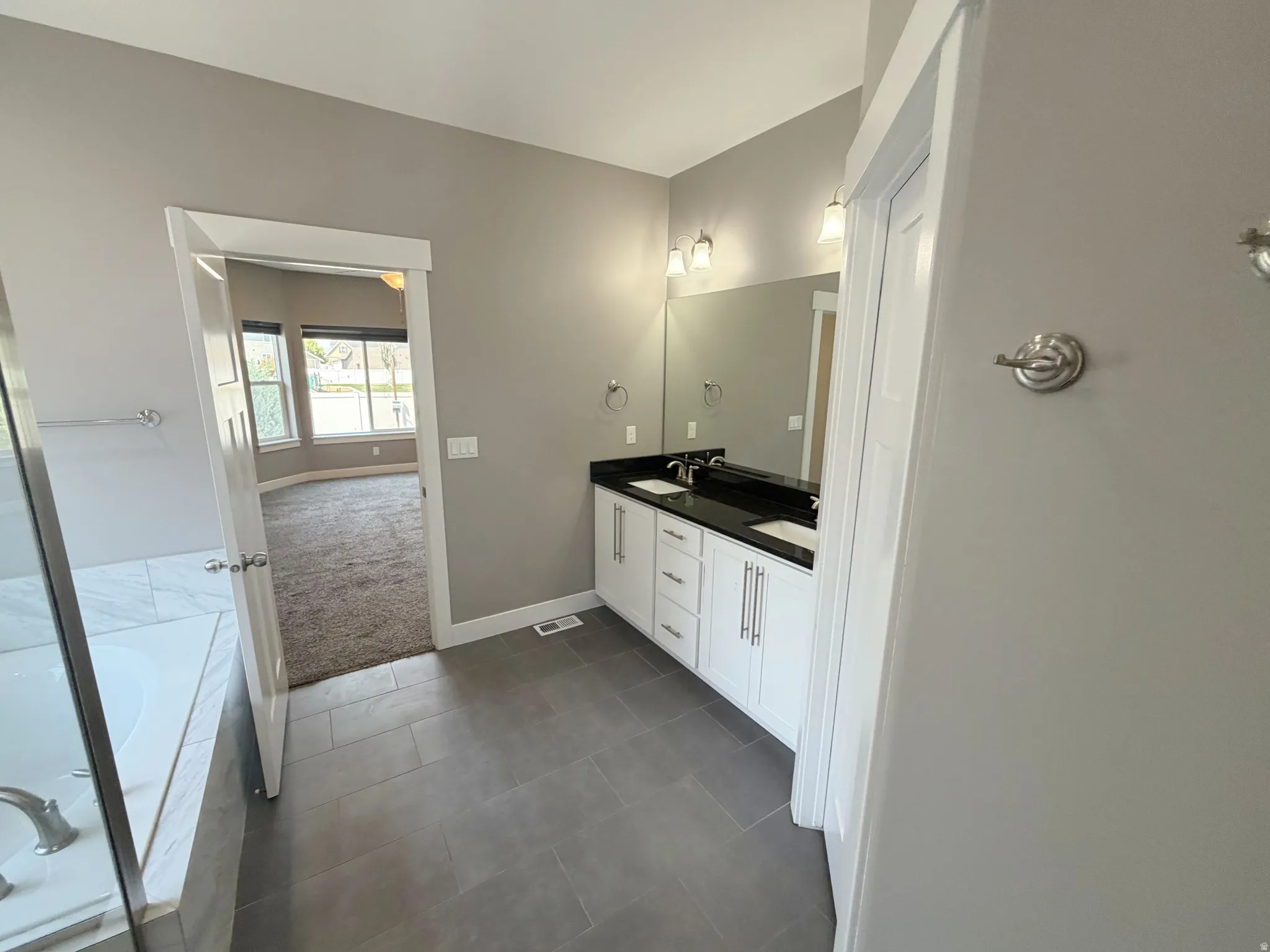 Modern bathroom featuring a double vanity with white cabinetry, dark countertops, and dual rectangular sinks