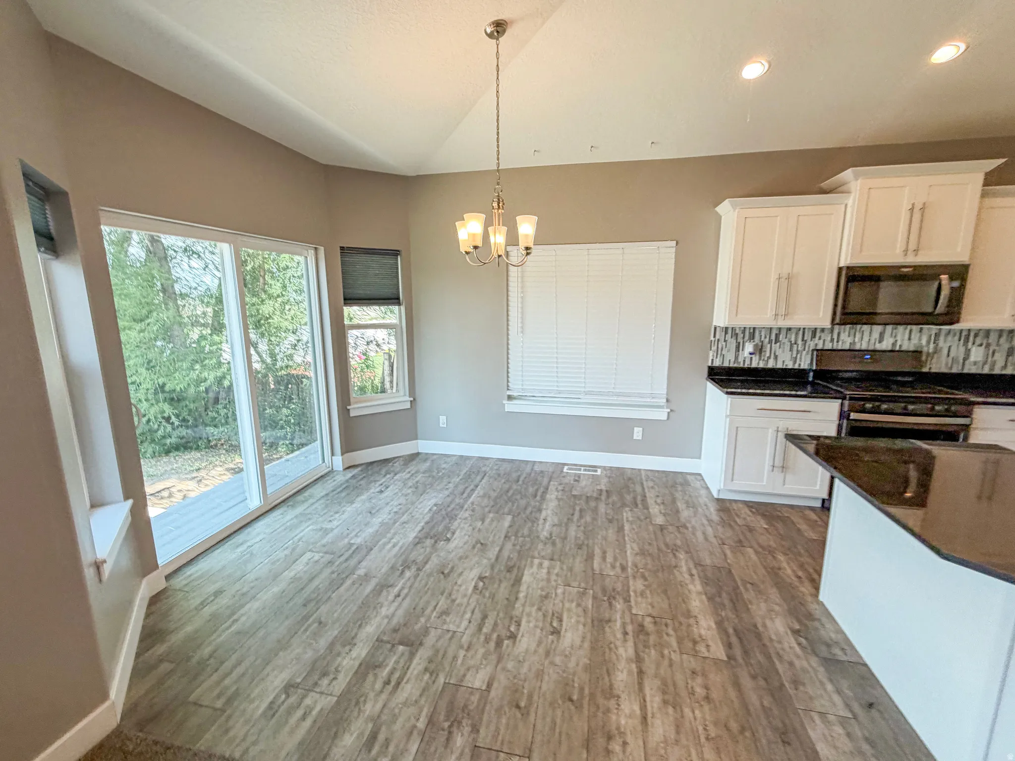 Open-concept kitchen and dining area featuring wood-finish flooring, vaulted ceiling, and recessed lighting