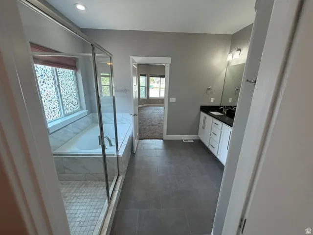 Modern bathroom featuring a glass-enclosed shower with tile flooring, a built-in tub with marble-finish surround, a dual vanity with a dark countertop and white cabinetry, and large format grey tile flooring
