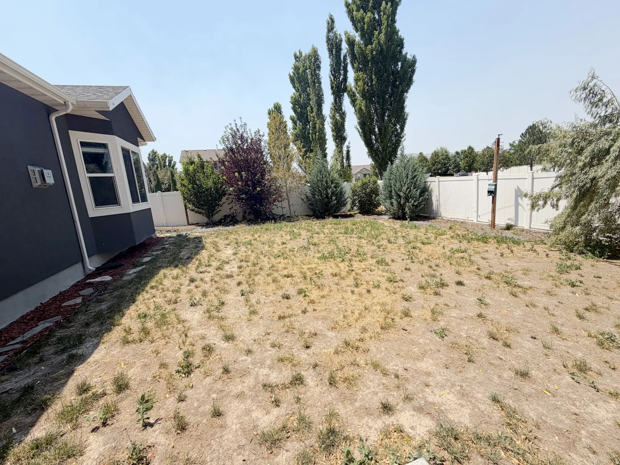 Expansive backyard featuring a privacy fence, mature trees, and a dark-colored exterior with bay windows