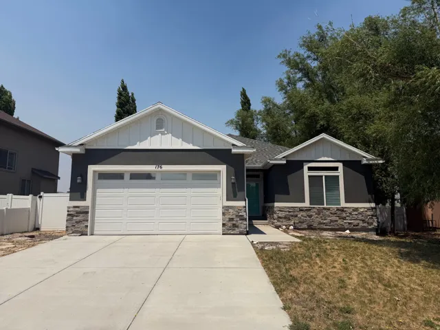 Contemporary-style exterior featuring a dark grey stucco finish, stacked stone accents, white trim, and a prominent two-car garage