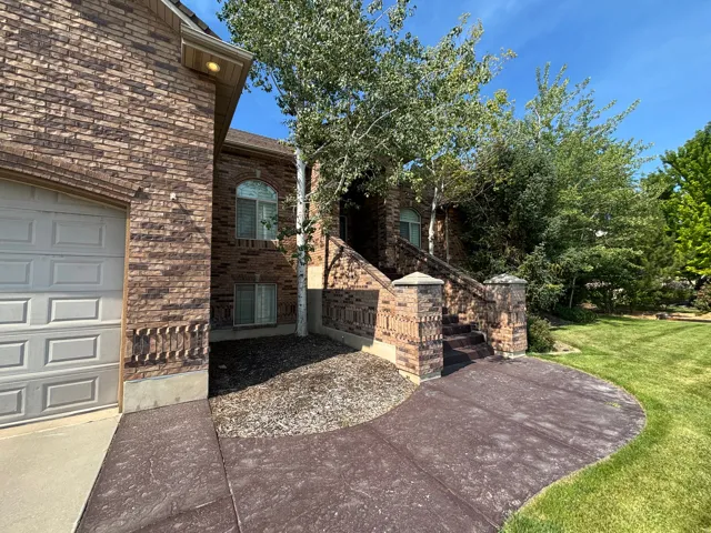 Brick exterior featuring an arched window, a two-car garage with a panel door, and a patterned concrete walkway leading to brick-capped steps