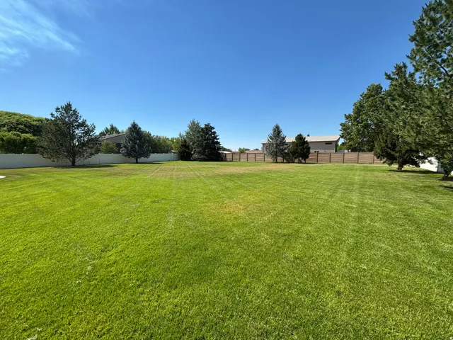 Expansive green lawn providing ample open space, bordered by a white privacy fence and mature trees
