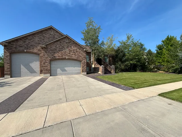 Brick facade home featuring a two-car garage, patterned concrete driveway, and expansive front lawn