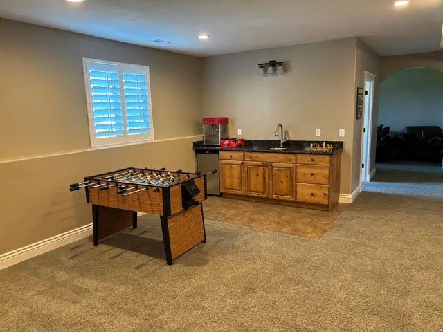 Versatile bonus room featuring recessed lighting, a window with white shutters, and a wet bar with wood cabinetry, a dark countertop, and a stainless steel sink
