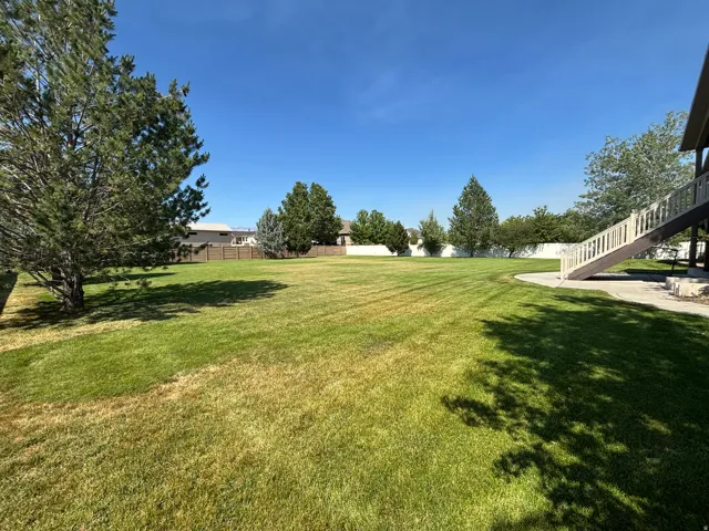 Expansive green lawn with mature trees and a multi-level deck featuring a staircase and white railings