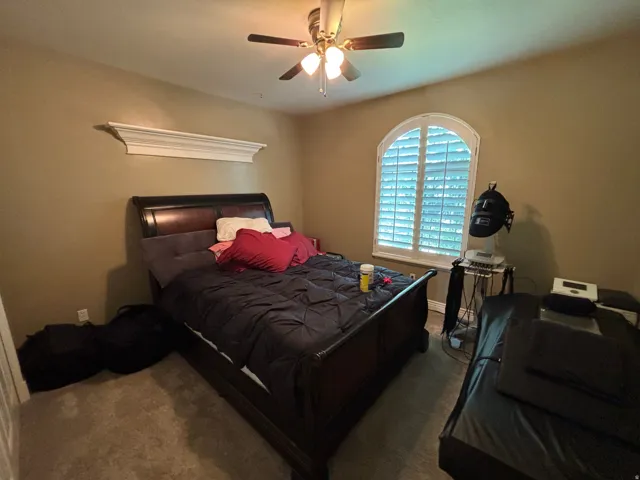 Bedroom featuring an arched window with plantation shutters, a decorative wall shelf, and a ceiling fan with integrated lighting