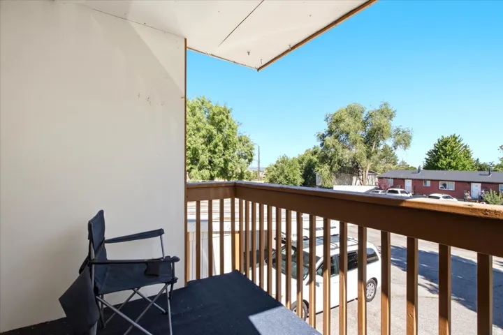 Outdoor balcony featuring a wooden railing, white exterior wall, and a dark floor surface