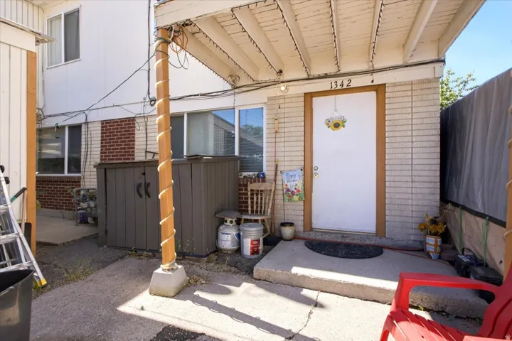 Covered entry with light-colored brick facade and a concrete patio