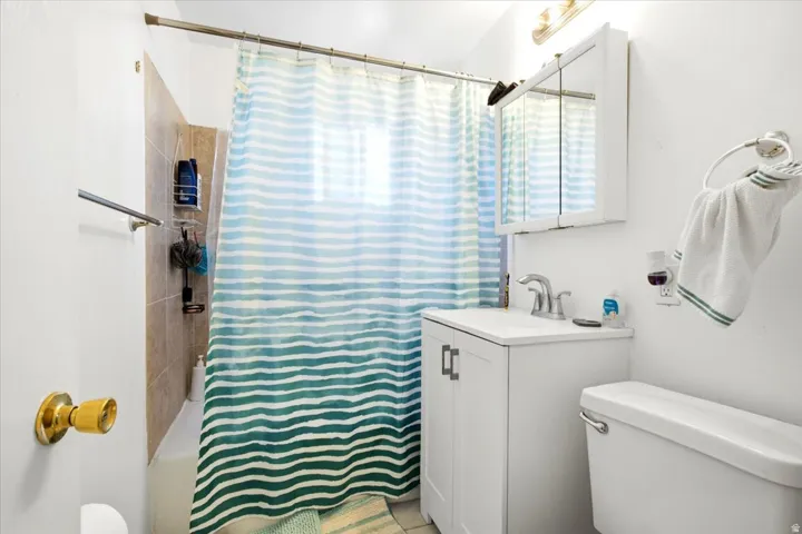 Bathroom featuring a shower/tub combination with tiled surround, a white vanity with integrated sink, a mirrored medicine cabinet, a toilet, and a wall-mounted light fixture
