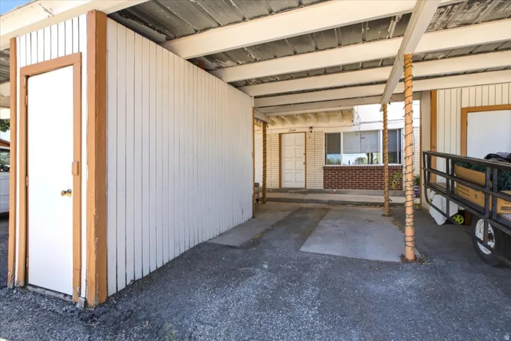 Covered carport featuring a storage room with white vertical panel siding and a white door with a brass-finish doorknob