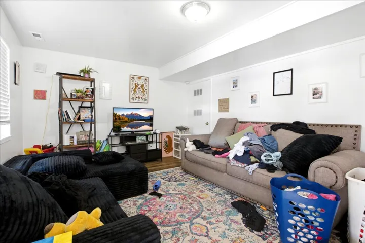 Spacious room featuring white walls, wood-finish flooring, and a decorative area rug