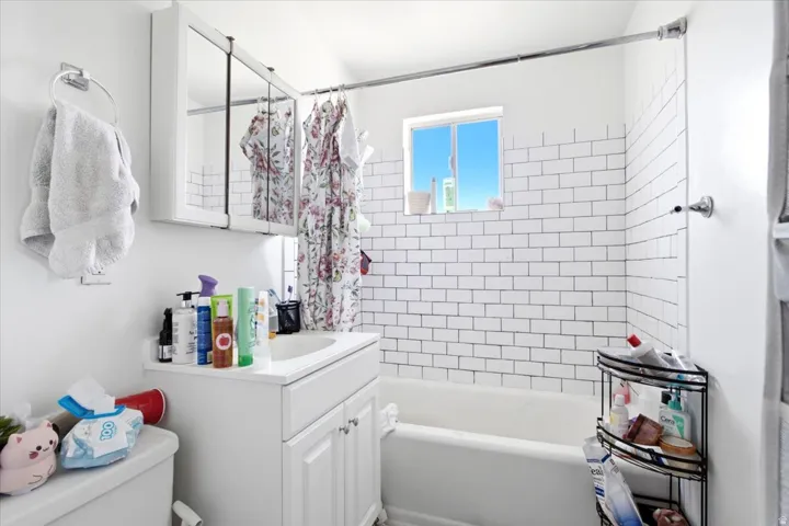 Bathroom featuring a white subway tile surround, a single window, white vanity with integrated sink, and a mirrored medicine cabinet