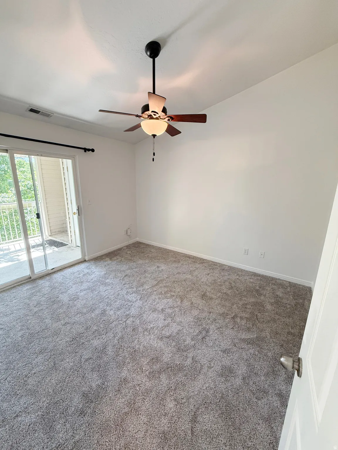 White walls, gray carpeting, and a ceiling fan with integrated lighting