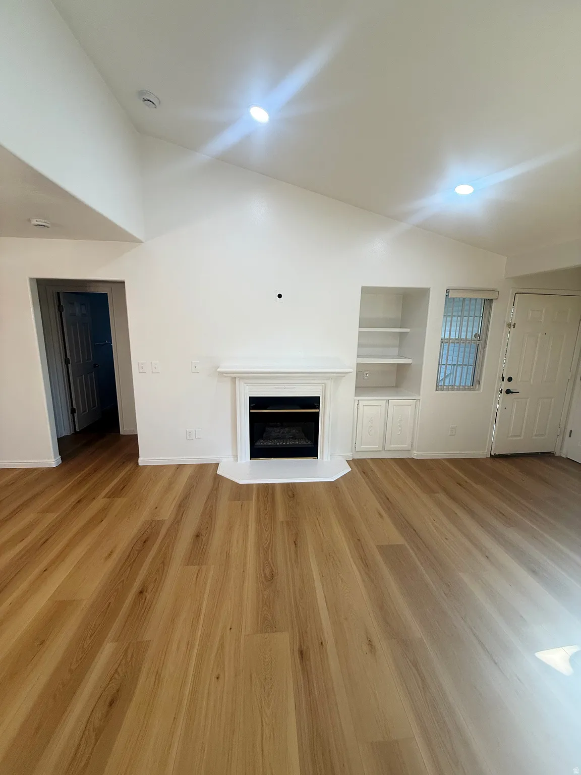 Living area featuring a white fireplace with a classic mantel, wood-finish flooring, built-in shelving, vaulted ceilings, and recessed lighting
