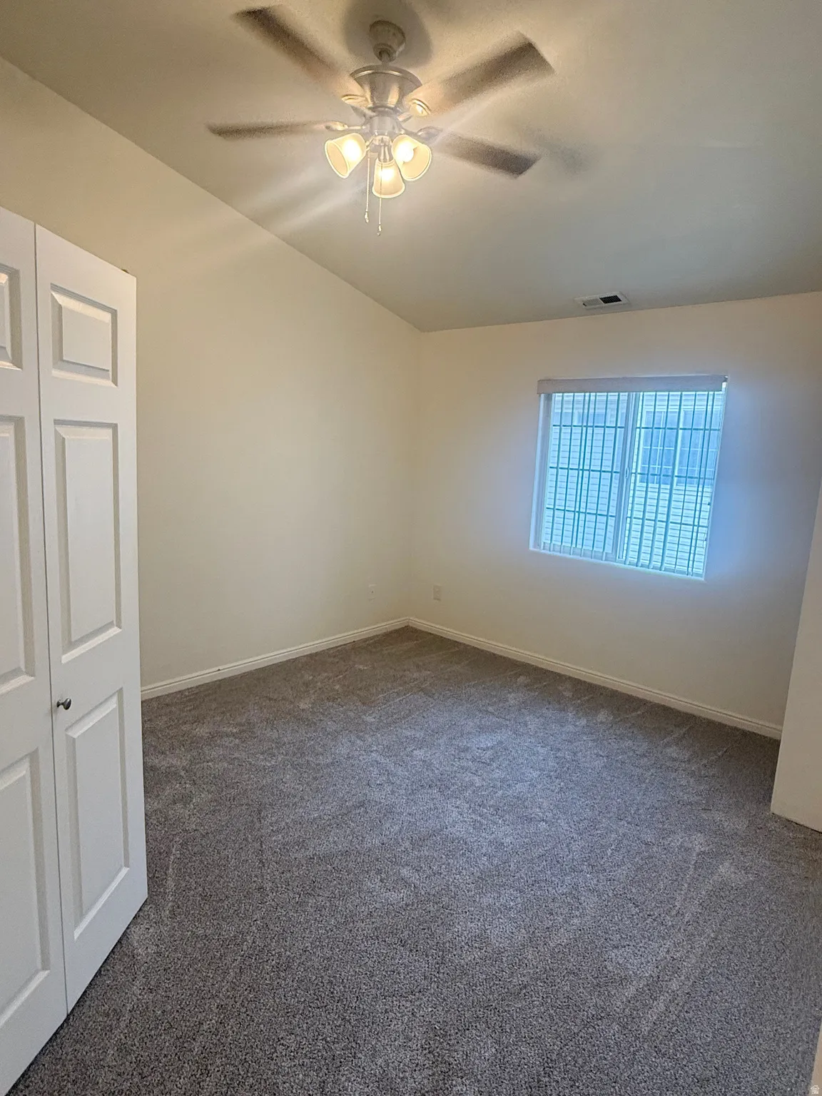 Bedroom featuring neutral wall paint, grey patterned carpeting, a multi-blade ceiling fan with integrated lighting, and a window with horizontal blinds and security bars