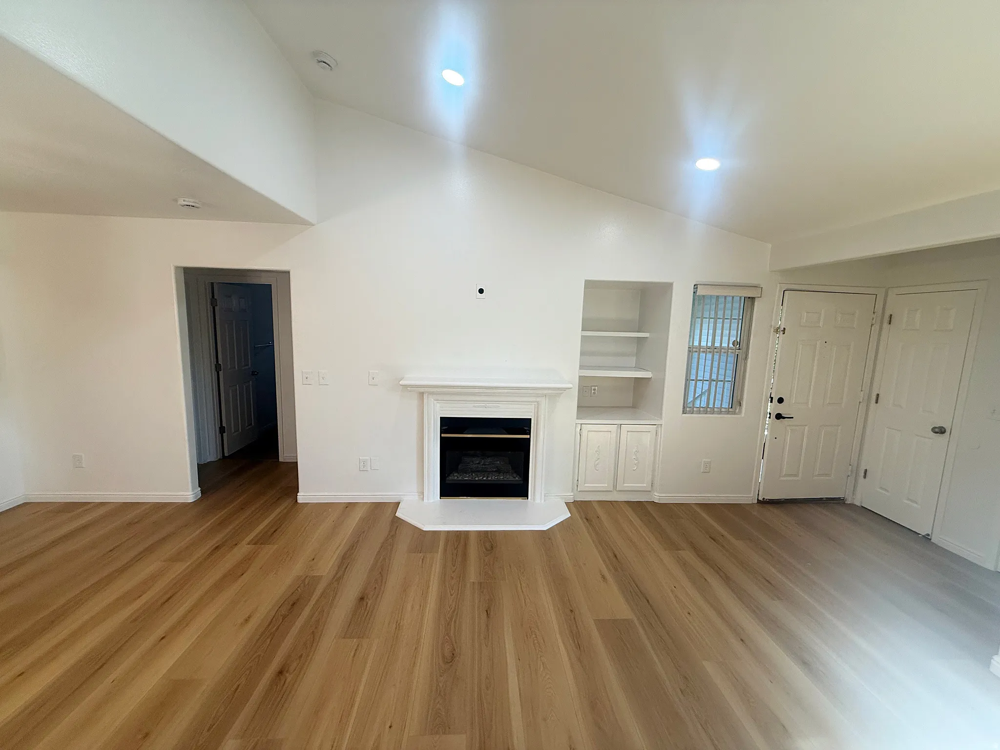 Spacious room featuring wood-finish flooring, a white mantel fireplace, vaulted ceilings, and recessed lighting