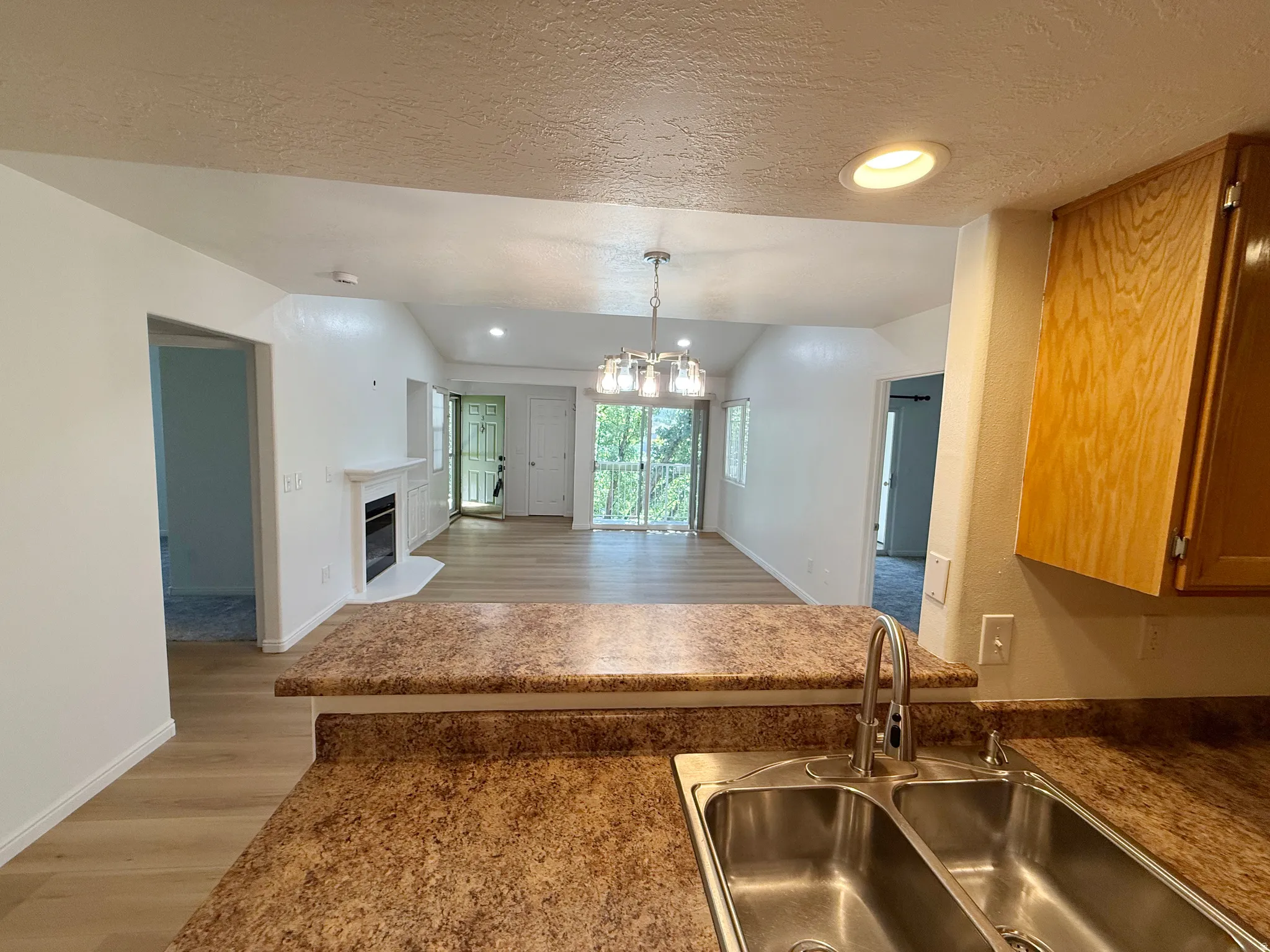 Kitchen pass-through with a dual basin stainless steel sink, speckled laminate countertops, and wood-finish cabinetry