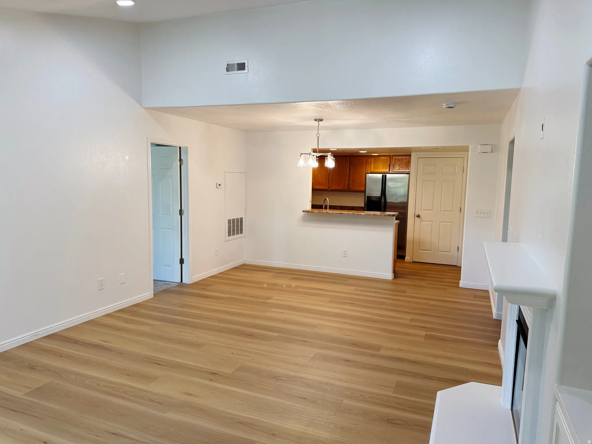 Vaulted ceiling, wood-finish flooring, white fireplace with mantle, breakfast bar with pendant lighting, and stainless steel refrigerator