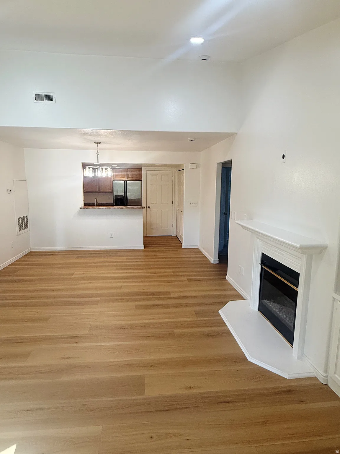 Spacious open-concept living area featuring wood-finish flooring, a white mantel fireplace, and vaulted ceilings