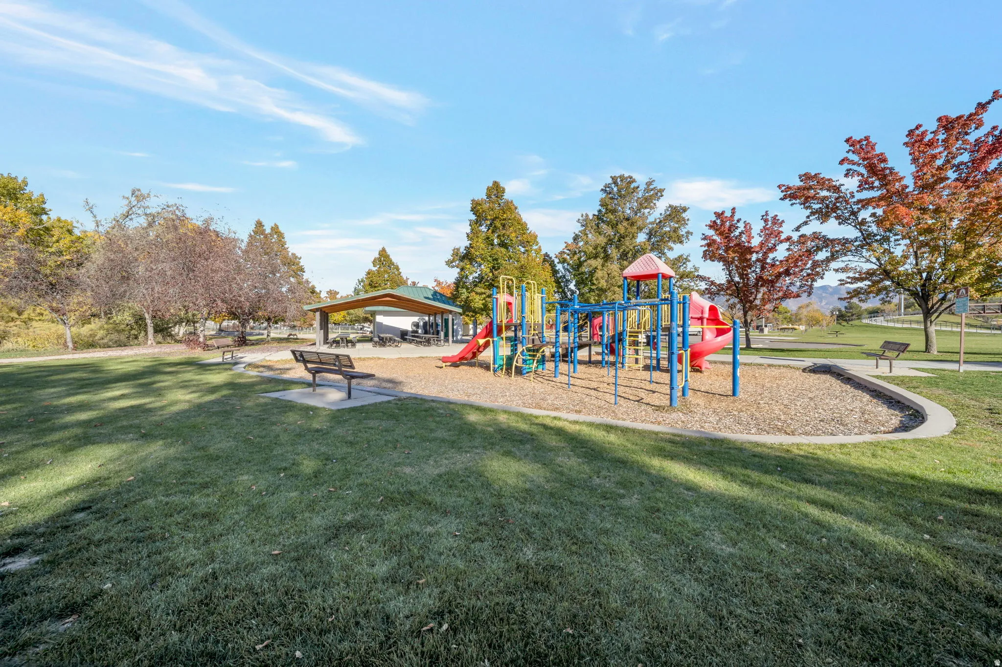 Expansive park area featuring a colorful playground, a covered picnic pavilion, and mature trees with autumn foliage