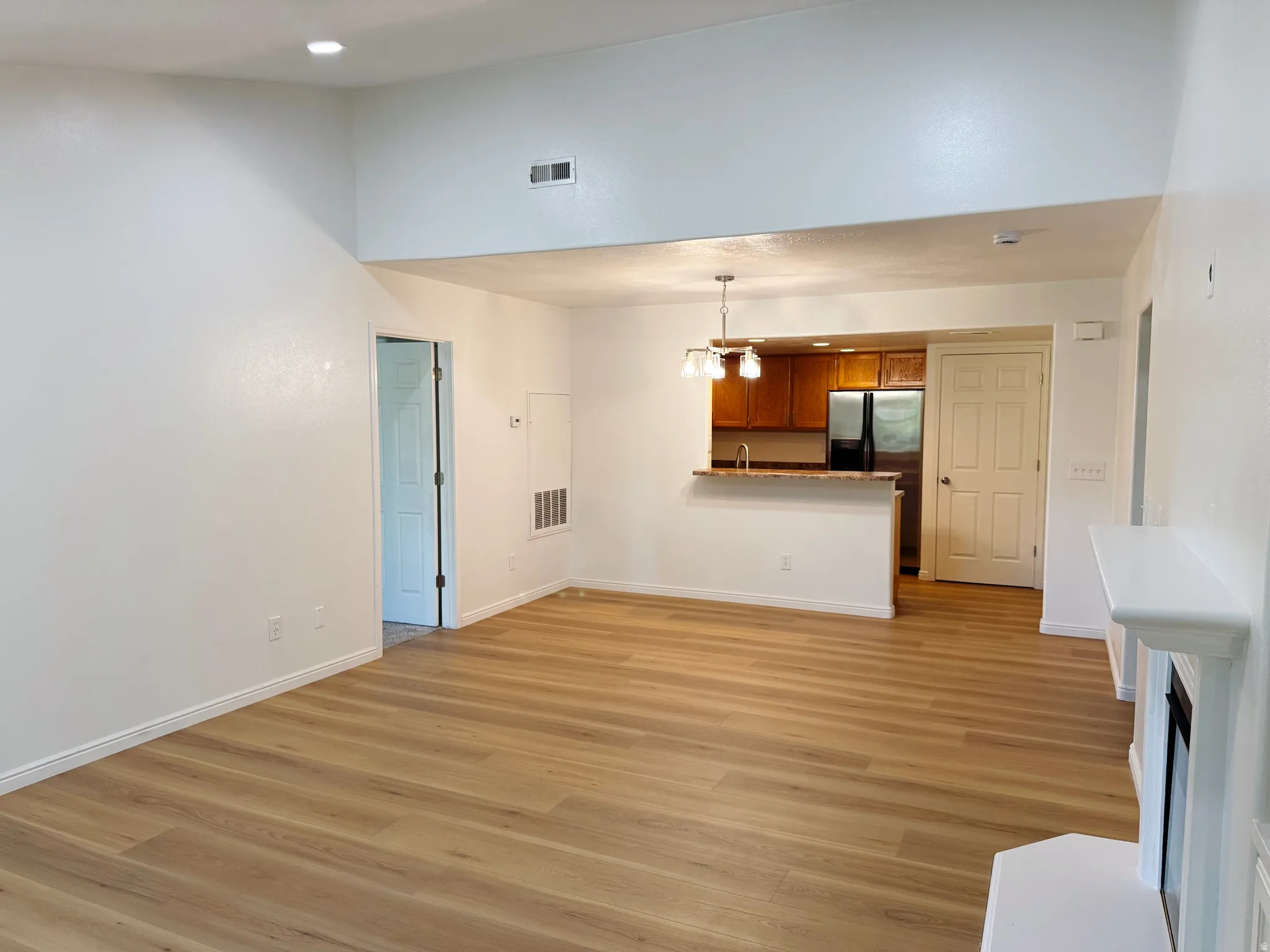 Vaulted ceiling, wood-finish flooring, kitchen bar with stone-look countertop, wood cabinetry, and a white mantelpiece