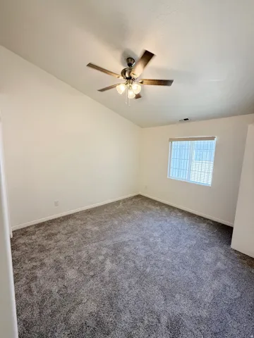 Vaulted ceiling with a ceiling fan, neutral carpeting, and a window with blinds