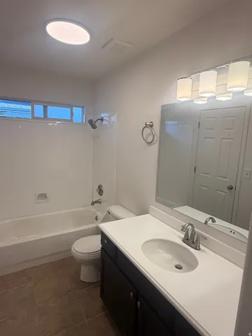 Bathroom featuring a dark wood-finish vanity with a white countertop and oval sink, a shower-over-tub combination with white subway tile surround, tiled flooring, and an overhead circular light fixture