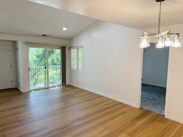 Vaulted ceiling, wood-finish flooring, sliding glass door with balcony, recessed lighting, and a contemporary chandelier