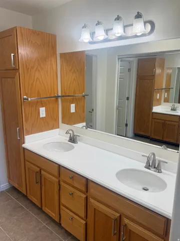 Double vanity with integrated white sinks and brushed nickel faucets set atop wood-finish cabinetry