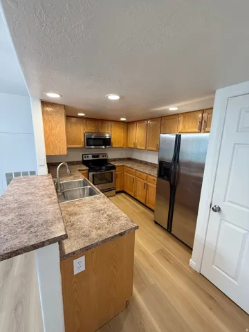 Recessed lighting illuminates wood-finish cabinetry, a stainless steel sink, and stainless steel appliances