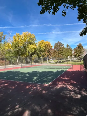 Regulation-size tennis court featuring a green and red playing surface, white court lines, and a black net