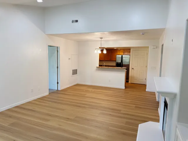 Vaulted ceiling, wood-finish flooring, white fireplace with mantle, breakfast bar with pendant lighting, and stainless steel refrigerator