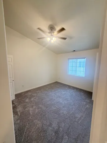Spacious interior room with vaulted ceilings and a ceiling fan with integrated lighting